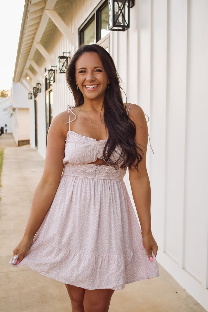 Blush dress featuring an ivory dotted pattern, a smocked waist, a cut out center bodice, a ruffled bottom hem, and adjustable straps!