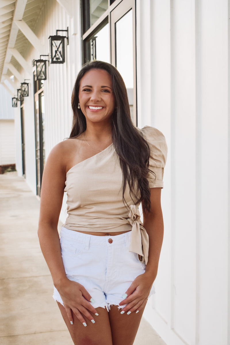 top in a neutral color, featuring cropped fit, smocked back hem, side zipper, one shoulder with puff sleeve and a front tie

