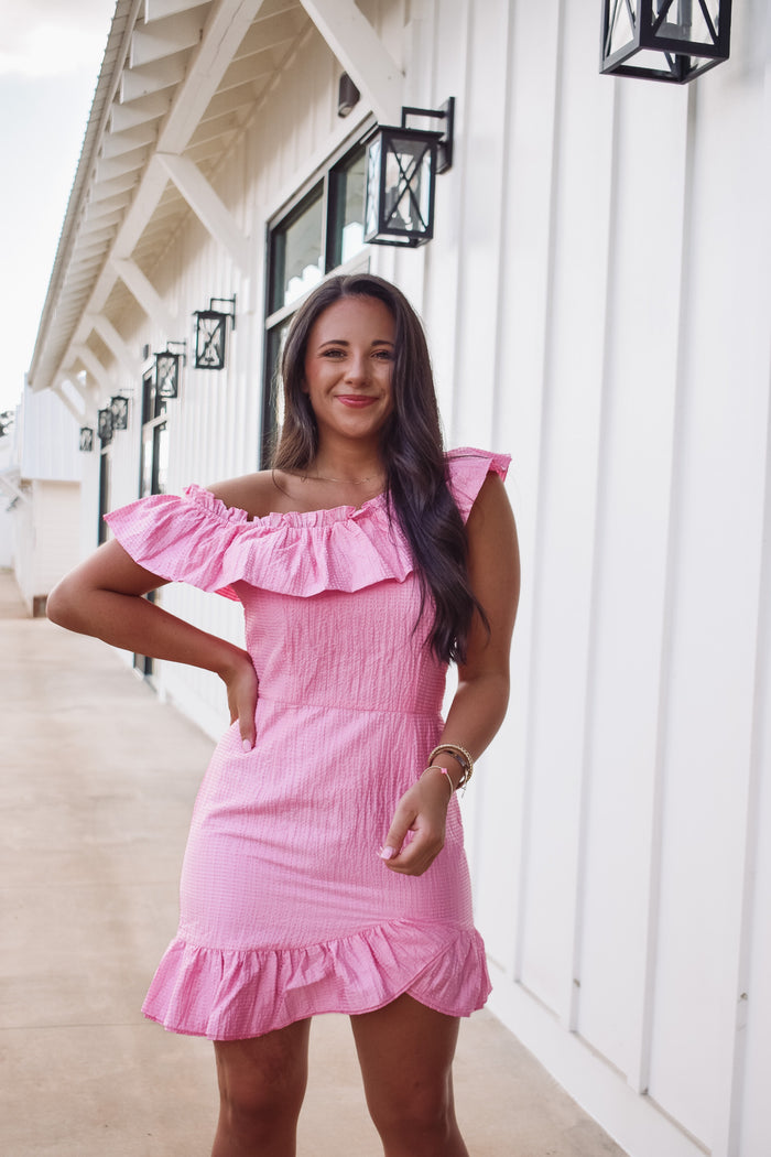 Gorgeous barbie pink asymmetrical dress,  featuring a textured fabric, ruffle accent along the neckline and tulip styled hem. 