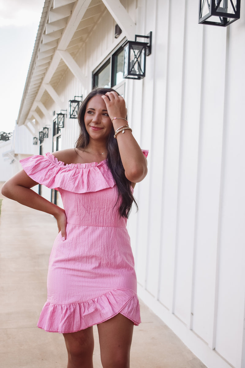 Gorgeous barbie pink asymmetrical dress,  featuring a textured fabric, ruffle accent along the neckline and tulip styled hem. 